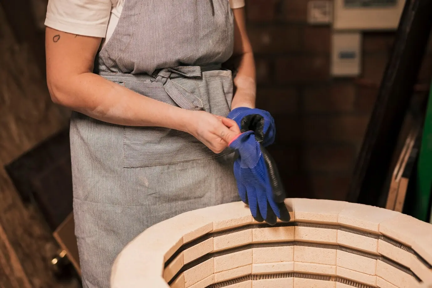 Nahaufnahme einer Töpferin, die in der Fabrik blaue Handschuhe trägt.